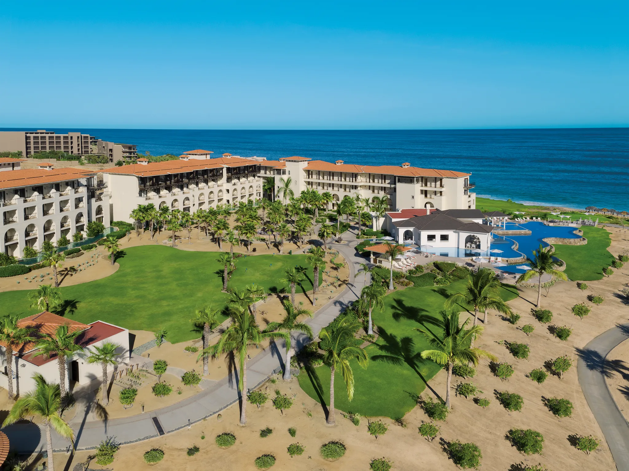 Aerial view of lush gardens and resort pool at Secrets Puerto Los Cabos Golf & Spa Resort overlooking the ocean.