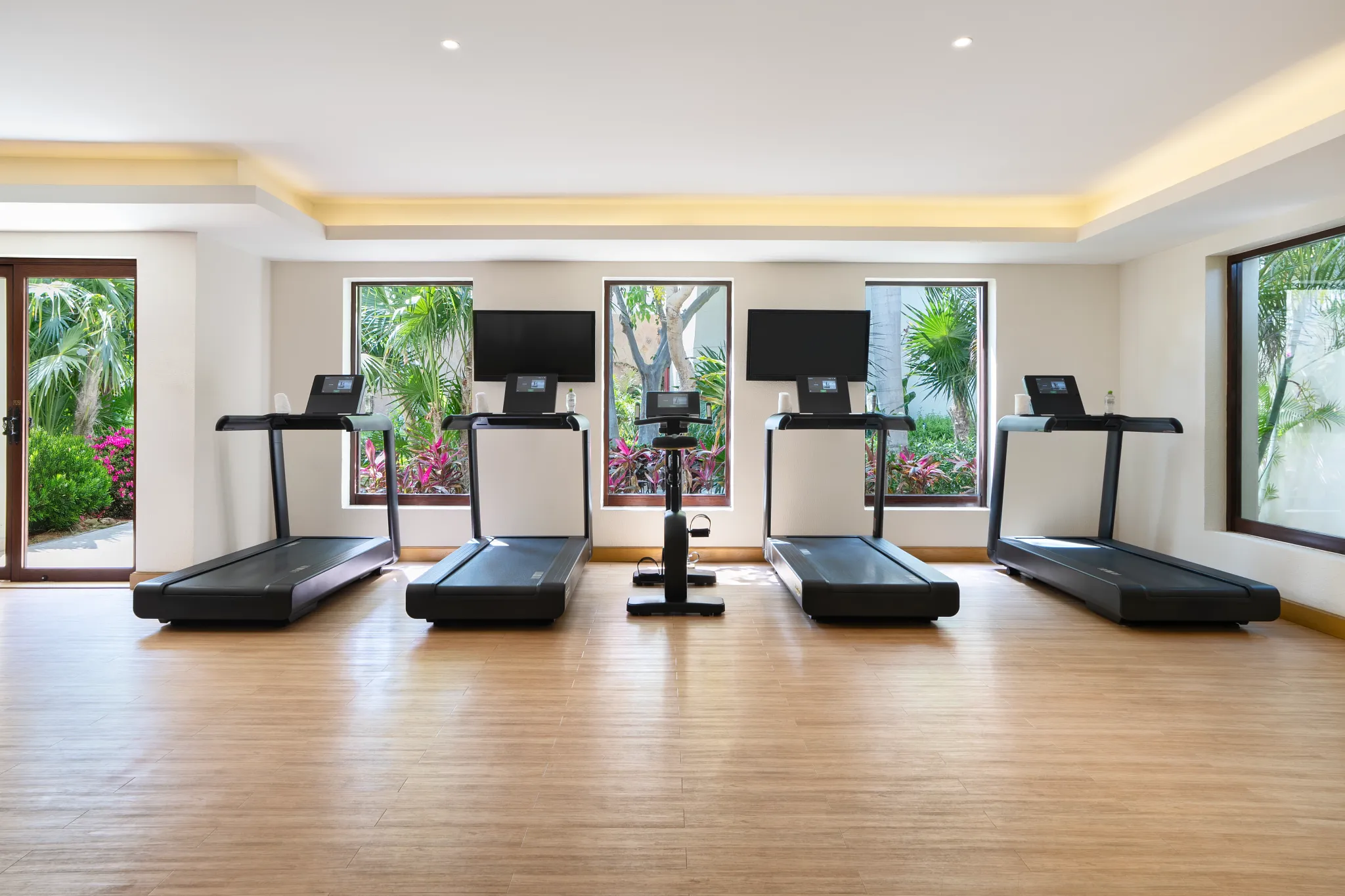 Row of treadmills and cardio machines with garden views at Secrets Puerto Los Cabos gym.