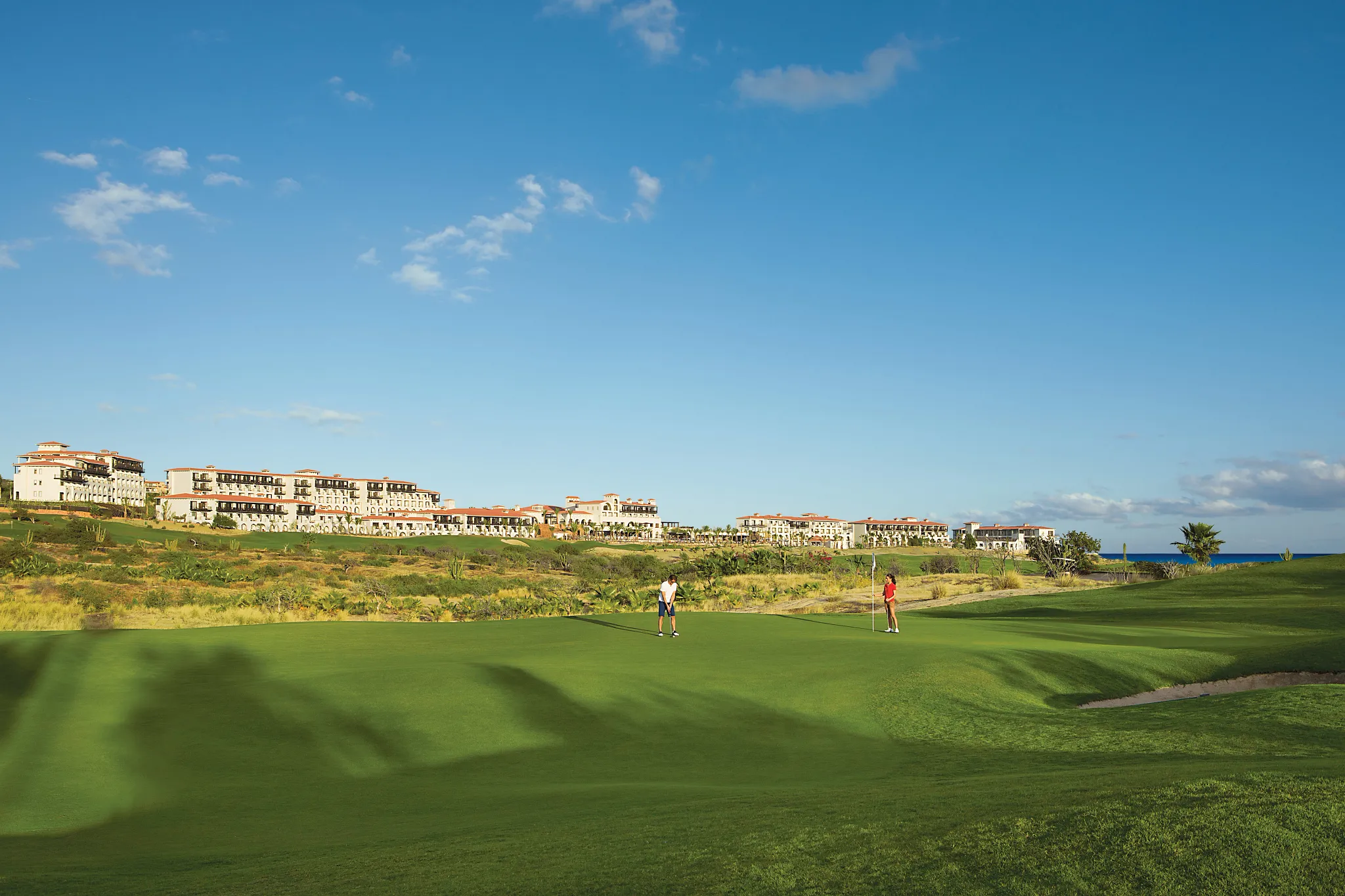 Golf course and resort buildings at Secrets Puerto Los Cabos with ocean views in the distance.